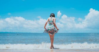 Summer 2026 Beauty - image of lady on beach dipping her toes in the sea wearing a dress